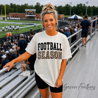 Model wearing sand Football Season graphic tee with black and leopard print letters at football stadium