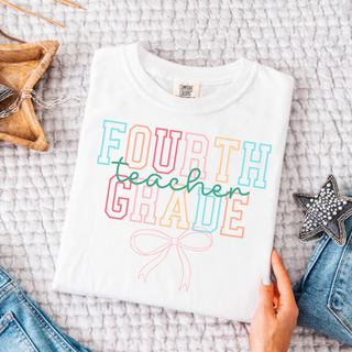 Folded white Fourth Grade Teacher bow graphic tee with colorful varsity lettering
