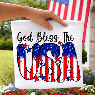Hand holding white tee outside with american flag showing god bless the usa flag letter design with red white and blue stars
