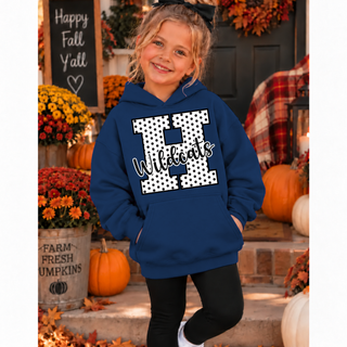 Girl in a navy hoodie with a white polka dot letter H outlined in black and black Wildcats script on the front, with plain sleeves, standing on a fall porch with pumpkins