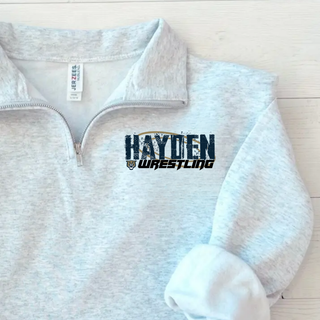 Close-up of an ash grey Jerzees cadet quarter-zip with Hayden in navy distressed block letters over a gold wrestling mat circle and Wrestling in black italic lettering on the left chest