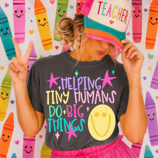 pepper grey adult graphic tee with helping tiny humans do big things teacher design, model wearing teacher hat with crayon background

