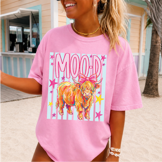 crunchberry Comfort Colors tee with highland moo-d cow and bow striped graphic, worn by smiling woman at a beach boardwalk

