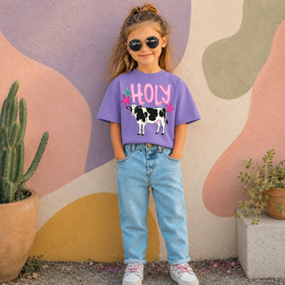 Young girl wearing lavender tee with holy pink text and black and white cow graphic, star accents
