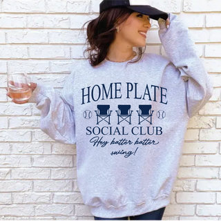 Model wearing sport grey crewneck with HOME PLATE SOCIAL CLUB Hey batter batter swing baseball chair design in navy
