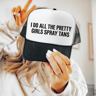 Woman holding a black and white foam front trucker hat with bold black text that reads I Do All The Pretty Girls Spray Tans