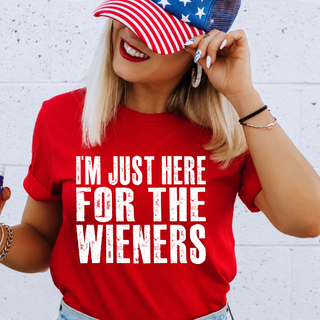 Woman wearing red I'm Just Here for the Wieners graphic top with American flag hat against white brick wall
