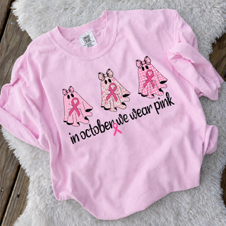 pink adult top with three pink ribbon ghosts and in october we wear pink text, flat lay on wood floor
