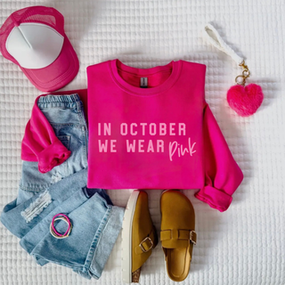 Bright pink Gildan crewneck with light pink In October We Wear Pink lettering styled with pink hat and denim
