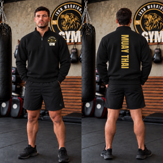 Man in a black cadet quarter-zip and black shorts in a gym, shown from the front and the back with Muay Thai in gold vertical lettering