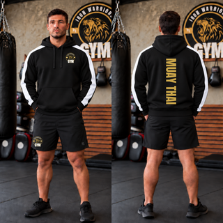 Man in a black hoodie with white shoulder panels in a gym, shown from the front with the Iron Warriors Gym lion crest on the left chest and from the back with Muay Thai in gold vertical lettering