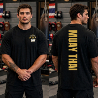 Man in a black tee with a round gold lion crest on the left chest, shown front and back, with a vertical gold Muay Thai print down the back