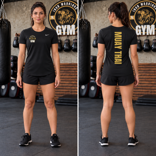 Woman in a black women's tee and black shorts in a gym, shown from the front with the Iron Warriors Gym lion crest on the left chest and from the back with Muay Thai in gold vertical lettering