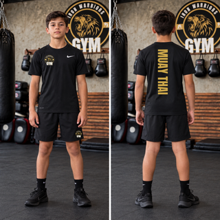 Boy in a black youth tee and black shorts in a gym, shown from the front with the Iron Warriors Gym lion crest on the left chest and from the back with Muay Thai in gold vertical lettering