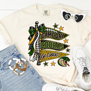 Jackson Heights Cobras Bow Pennant Top, three stacked Game Day, Cobras, and Go Cobras! pennant banners with a ribbon bow and cobra head icon, on an ivory tee