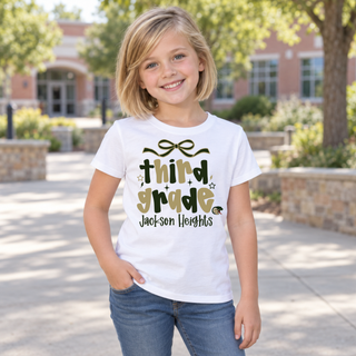 Girl wearing Jackson Heights Cobras Third Grade Bow Top in white featuring third grade bubble lettering with a bow accent, sparkles, Jackson Heights script, and a cobra head icon