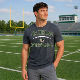 Male model wearing a dark heather grey Jackson Heights Jr. Cobras Victory Arch Gildan T-shirt on a football field