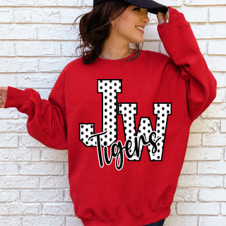Woman in a red crewneck sweatshirt and black cap with white polka dot JW letters outlined in black and black Tigers script on the front, standing against a white brick wall
