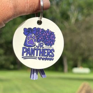 Jr. Panthers Cheer round keychain with purple tassel displayed outdoors