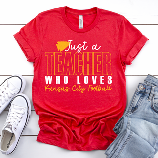 Red tee with Just a Teacher Who Loves Kansas City Football design, flat lay with white sneakers and distressed denim
