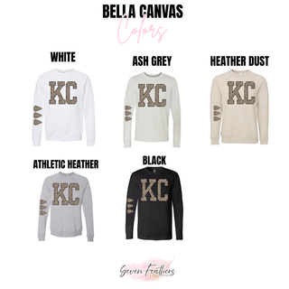 Bella Canvas crewneck sweatshirts and long sleeve tees in white, ash grey, heather dust, athletic heather, and black with KC lettering in leopard print and leopard print arrowheads on the sleeve