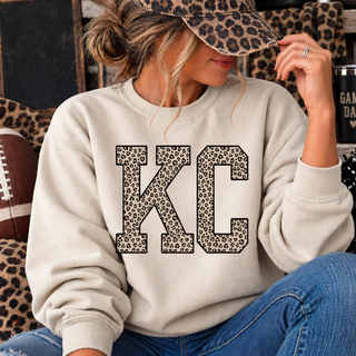Cream crewneck sweatshirt with KC lettering in leopard print and black outline, worn by a model