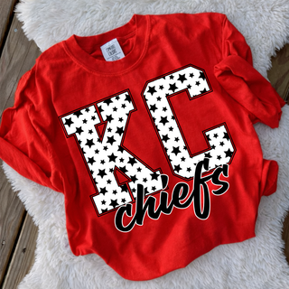 red adult top with black and white star pattern kc lettering laid on wood floor with fur rug
