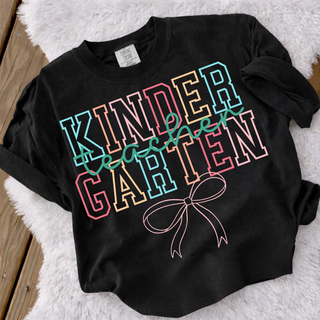Black adult Kindergarten Teacher Bow Comfort Colors graphic tee with colorful varsity letters