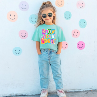 Girl wearing chalky mint tee with KNOW YOUR WORTH colorful daisy pop patchwork letters, smiley face, stars, adult
