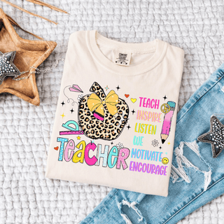 Ivory Comfort Colors tee folded flat with TEACHER teach inspire listen we motivate encourage leopard apple bow design
