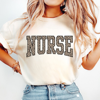 Woman wearing ivory Leopard Print Nurse Graphic Top with bold varsity NURSE lettering in leopard print