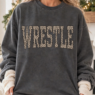 Close-up of a dark charcoal Comfort Colors style crewneck sweatshirt with the word Wrestle in bold block letters filled with a tan and brown leopard print and outlined in black