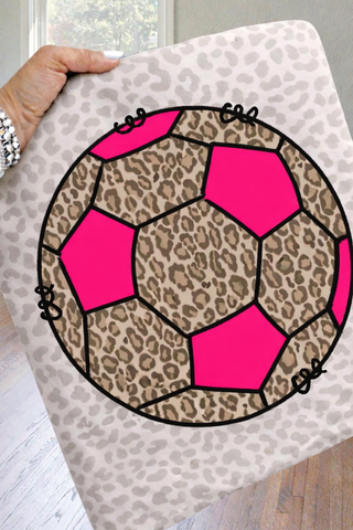 Hand holding a leopard print LAT fine jersey tee with a large hot pink and leopard print soccer ball graphic