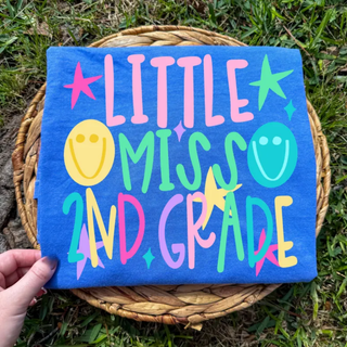 Little Miss 2nd Grade graphic tee in flo blue folded with colorful lettering, stars, and smiley faces
