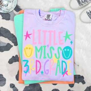 Little Miss 3rd Grade graphic tee in lavender folded with colorful lettering, stars, and smiley faces
