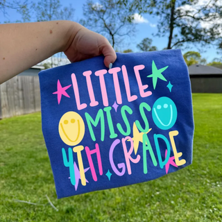 Little Miss 4th Grade graphic tee in true navy held outdoors with colorful lettering, stars, and smiley faces
