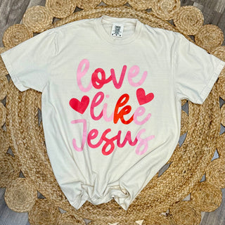 Ivory Comfort Colors tee laid flat on wicker with love like Jesus ombre script and hearts graphic
