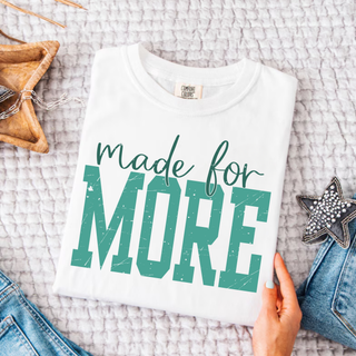 White Comfort Colors tee with made for MORE distressed varsity block and script design laid flat with denim

