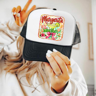 Woman holding a black and white trucker hat with Margarita Weather margarita glass bow and tropical graphic on the front panel
