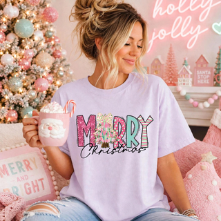 Model wearing a lavender tee with MERRY lettering in festive patterns, a Christmas tree, and Christmas script.