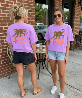 Two women outside wearing the Monkey See Monkey Do Graphic Tee in violet showing front and back monkey star design