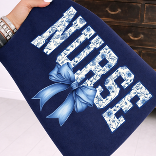 Hand holding true navy top with NURSE blue chinoiserie floral letters and coquette bow, adult unisex