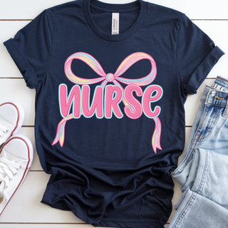 Navy tee laid flat with a large coquette bow above nurse in pink bubble script graphic on the front
