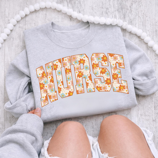 Folded ash grey crewneck with NURSE arched daisy floral print letters in orange blue retro flowers, youth adult unisex
