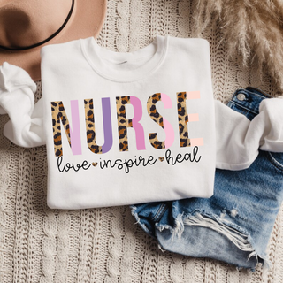 White crewneck sweatshirt with leopard print NURSE love inspire heal graphic design laid flat with hat and denim