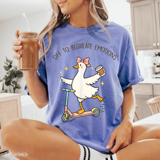 Woman wearing a periwinkle Comfort Colors tee with a cartoon goose riding a scooter holding coffee and the words off to regulate emotions