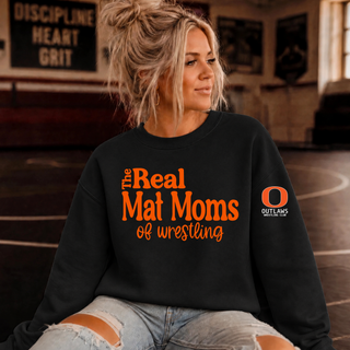 Woman in a black crewneck sweatshirt in a wrestling room with orange The Real Mat Moms of wrestling lettering on the front and an orange Outlaws Wrestling Club O logo on the sleeve