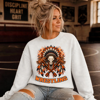 Woman in a white crewneck sweatshirt in a wrestling room wearing the Ogden's Outlaws Wrestling feathered bull skull and crossed axes graphic with orange WRESTLING lettering