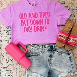 Orchid Comfort Colors tee flat lay with old and tired but down to day drink pink graphic, jeans and sandals
