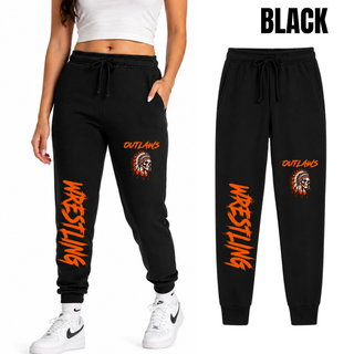 Woman wearing black fleece joggers beside a flat black pair, with Outlaws and a feathered skull on the thigh and large orange Wrestling lettering down the lower leg